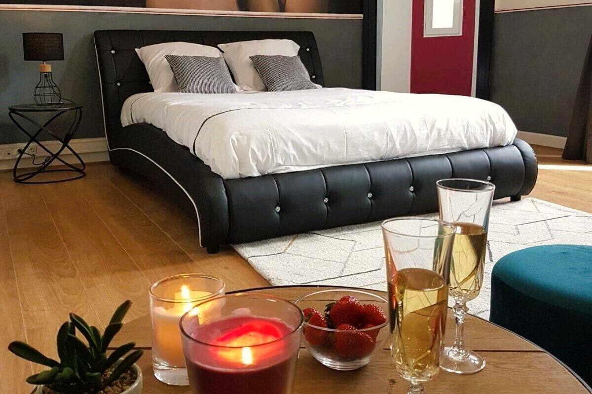 Quarto moderno com cama estofada preta, roupa de cama branca, mesa de cabeceira com abajur e uma pequena planta em vaso.