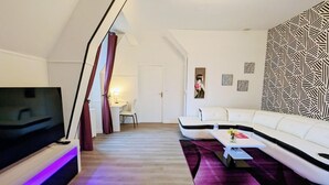 A modern living room with a flat-screen TV, a white sofa, a coffee table, and a patterned wall. - Chateau de la Rose (Cluis)