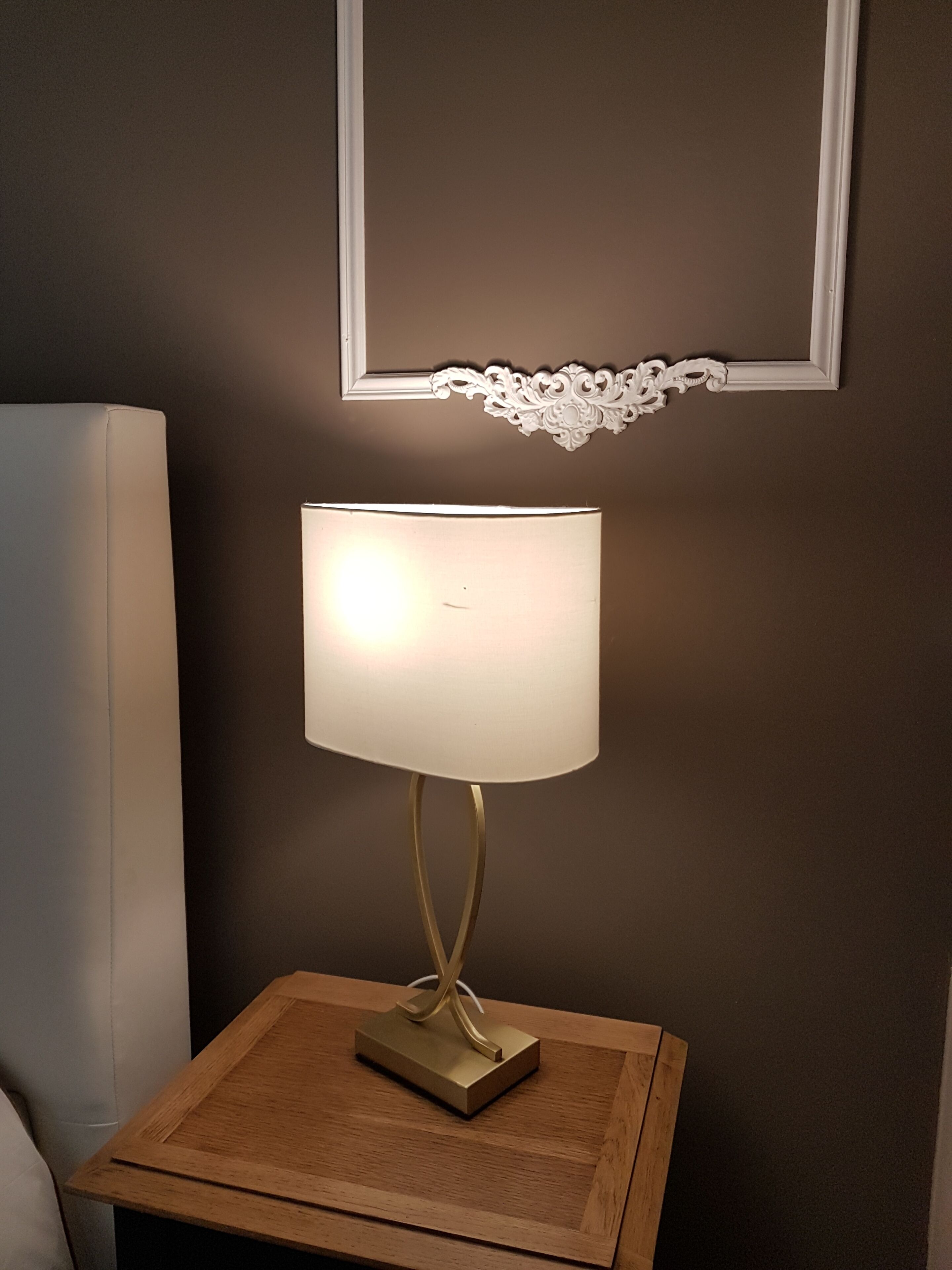 Una mesita de noche con lámpara, un cuadro enmarcado arriba y un mueble blanco junto a la cama.