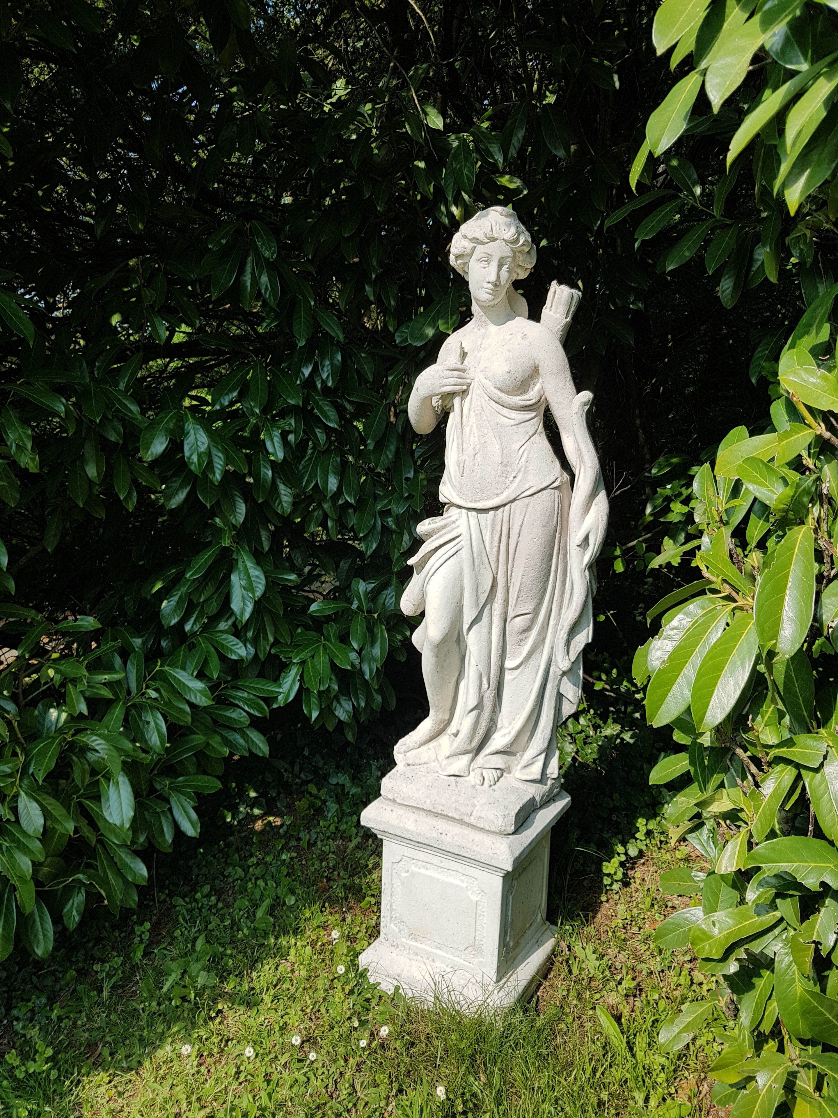 A statue of a woman in a garden with lush green foliage in the background.