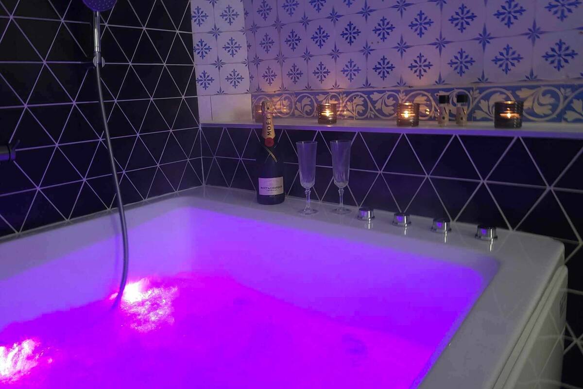 Uma banheira com luz roxa, uma garrafa de champanhe e velas em uma prateleira.