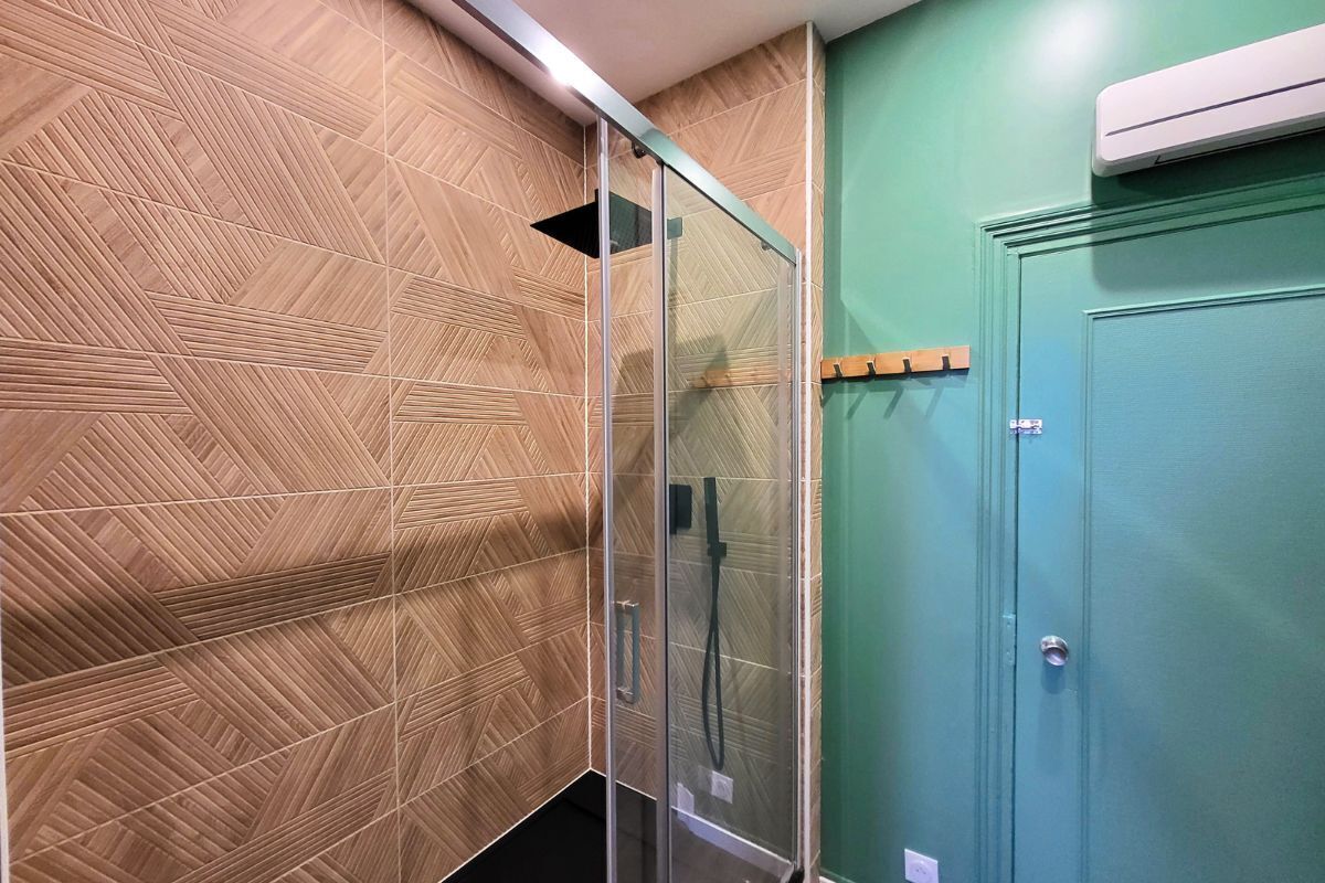 A bathroom with a geometric patterned wall, a glass shower enclosure, and a teal door.