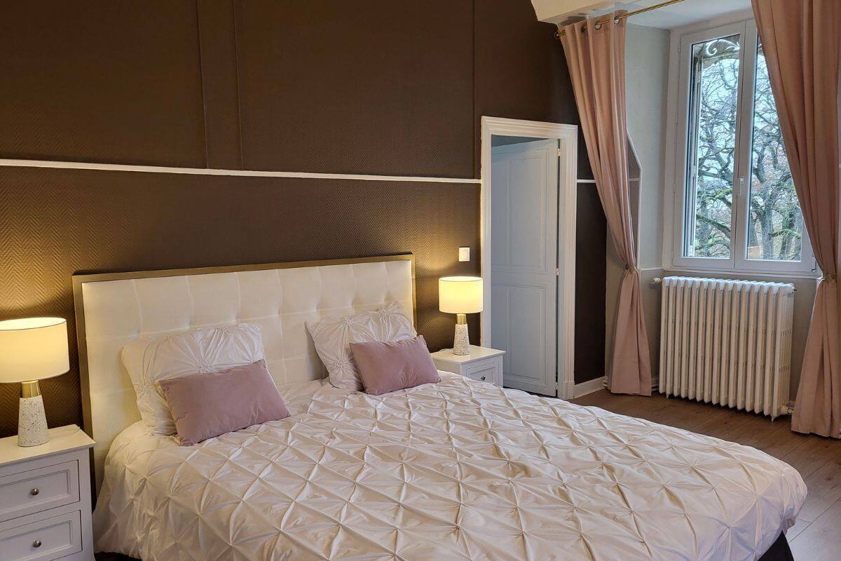 Quarto com uma cama grande, duas mesas de cabeceira com abajures, um radiador e uma janela com cortinas.