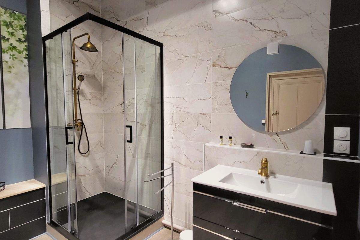A modern bathroom with a glass-enclosed shower, a white sink, and a marble-tiled wall.