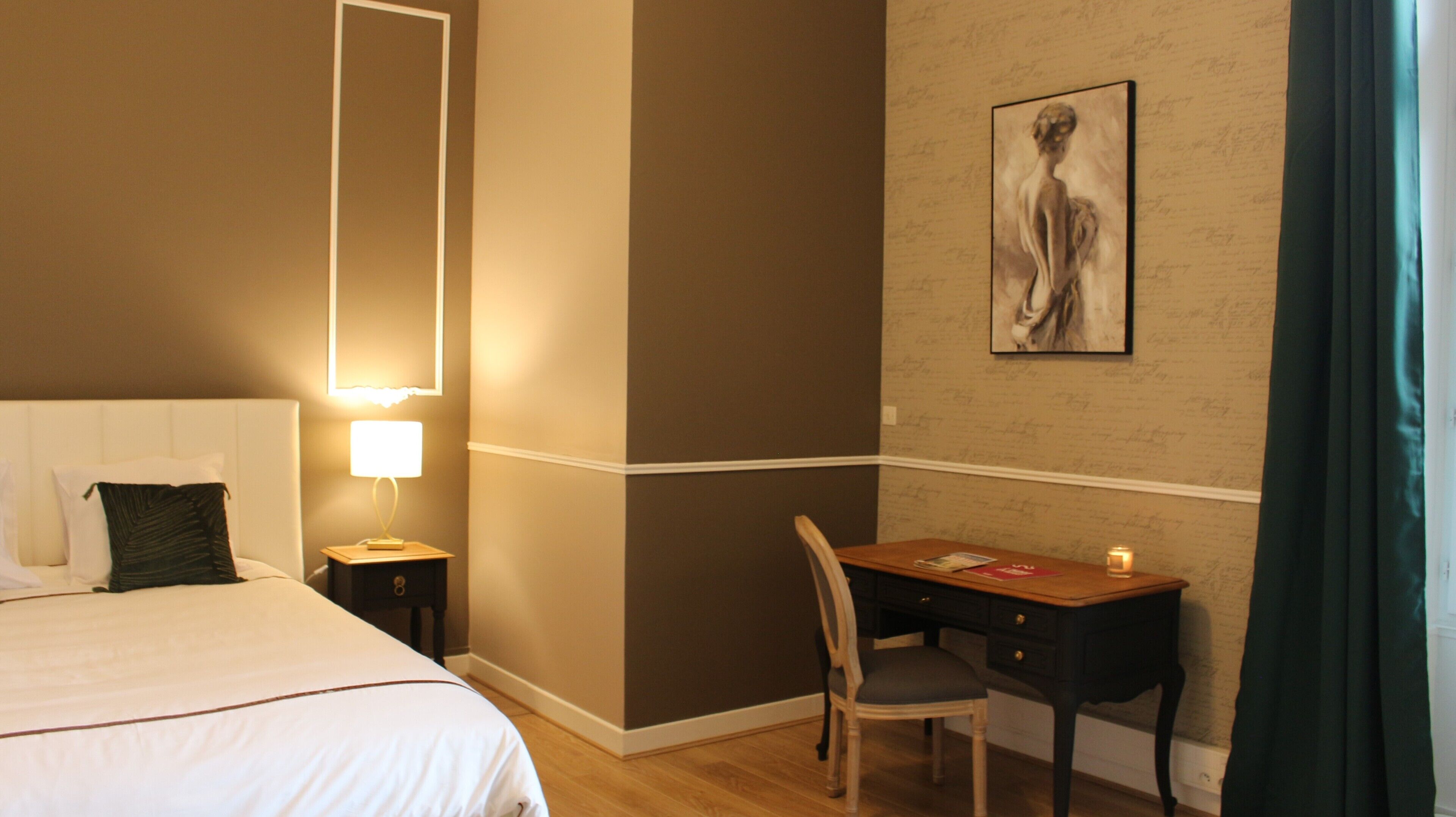 Habitación de hotel con cama, mesita de noche, lámpara, escritorio, silla y un cuadro en la pared.