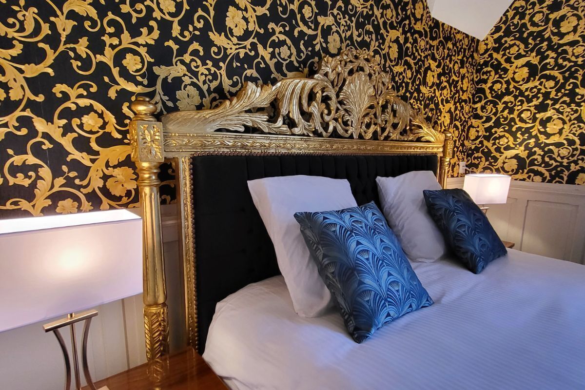 A luxurious bedroom with a large bed, ornate headboard, and patterned wallpaper.