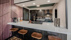 A modern kitchen with a white countertop, dark cabinets, and a central island with stools. - Finger Lakes Escape • FLX Chalet + Private Pond (Branchport)