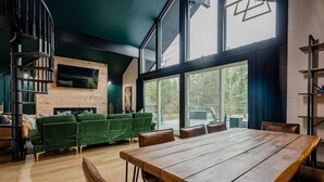 A modern living room with a wooden dining table, green sofa, and a fireplace. - Finger Lakes Escape • FLX Chalet + Private Pond (Branchport)