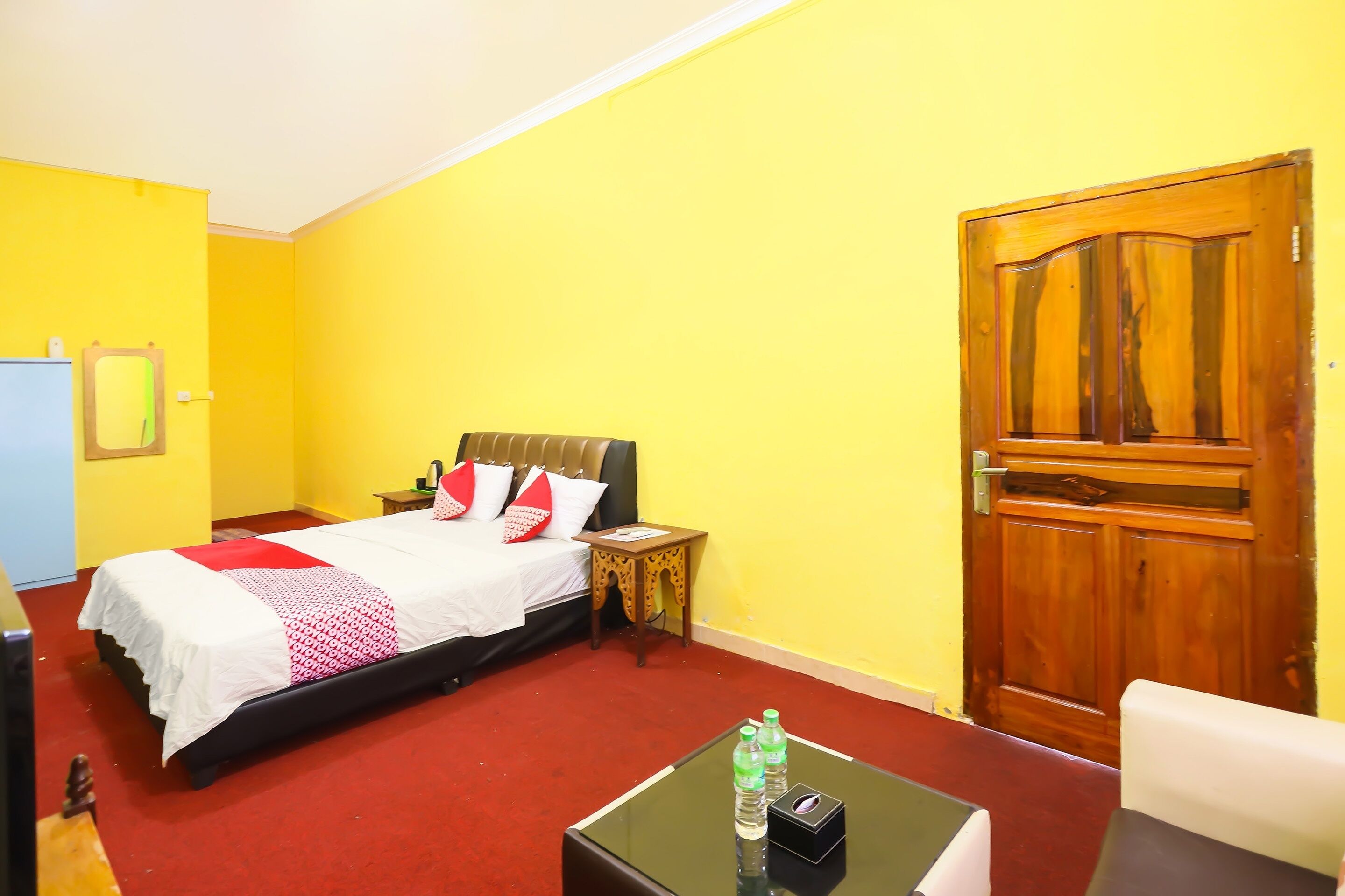 A hotel room with a bed, a nightstand, a wooden door, and a small table with two bottles.