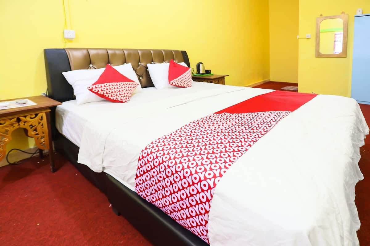 Hotellihuone, jossa on sänky, yöpöytä, puinen kaappi ja keltainen seinä.