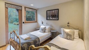 A bedroom with two beds, a window with a view of greenery, and a framed picture on the wall.