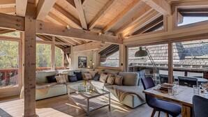 A spacious living area with a high ceiling, wooden beams, a sofa set, a glass coffee table, and a dining table with chairs.