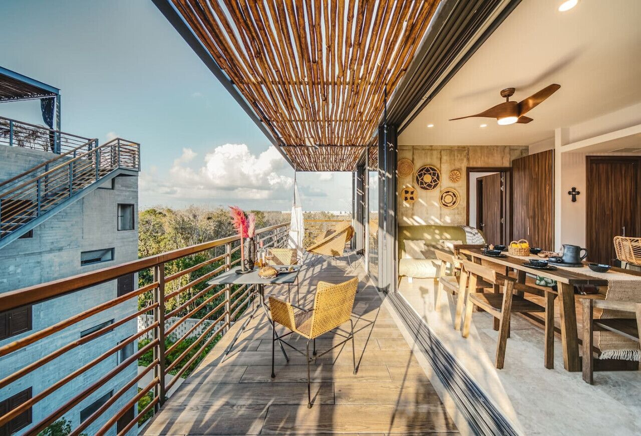 A modern balcony with a wooden ceiling, a dining area with wooden furniture, and a staircase leading to an upper level.