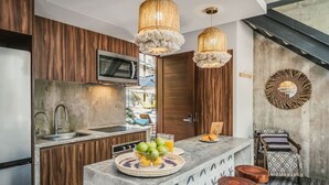 A modern kitchen with wooden cabinets, a built-in microwave, a large island with a fruit bowl, and pendant lights.