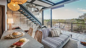 A modern interior with a dining area, sofa, and staircase leading to a balcony with a view. - Tulum Paradise: Penthouse w/ Private Pool & Cenote (Tulum)