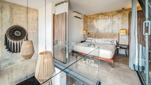 A modern bedroom with a glass partition, a bed with white linens, two bedside lamps, and a decorative wall hanging. - Tulum Paradise: Penthouse w/ Private Pool & Cenote (Tulum)