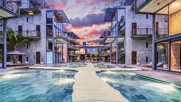 A modern hotel with a central pool, multiple balconies, and a sunset sky. - Tulum Paradise: Penthouse w/ Private Pool & Cenote (Tulum)