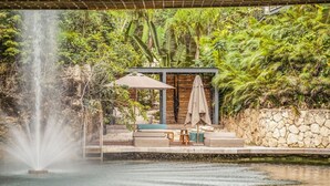 A serene outdoor area with a waterfall, a stone wall, and a seating area with a table and chairs. - Tulum Paradise: Penthouse w/ Private Pool & Cenote (Tulum)
