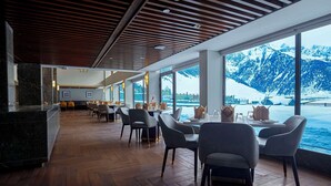 A restaurant with wooden flooring, modern chairs, and large windows offering a view of snow-capped mountains. - Radisson Hotel Sonamarg (Gund)