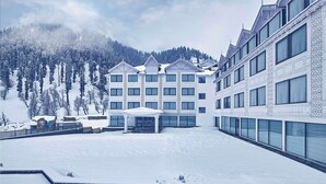 A hotel with multiple floors, a covered entrance, and a snow-covered landscape with trees and mountains in the background. - Radisson Hotel Sonamarg (Gund)