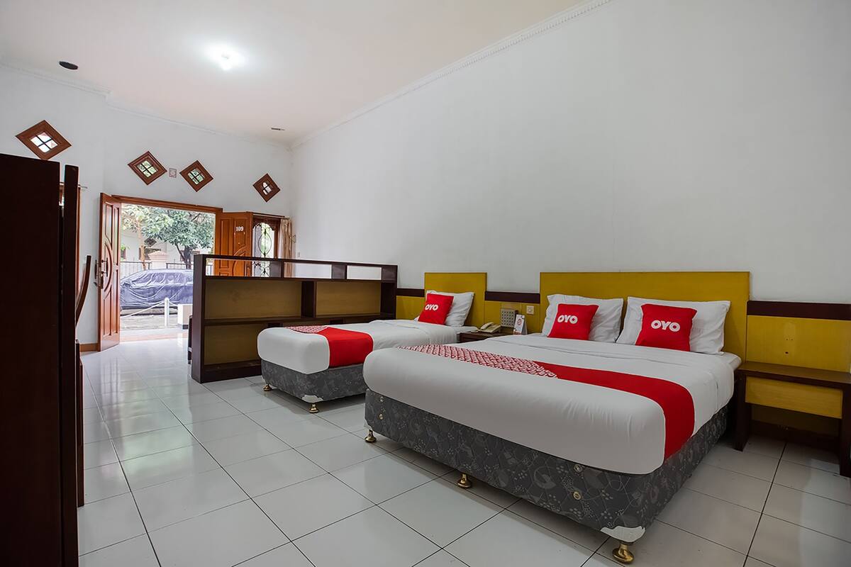 A hotel room with two beds, a wooden headboard, a nightstand, and a door leading to a balcony.