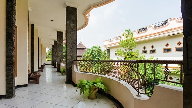 A covered balcony with tiled flooring, stone pillars, and a wrought iron railing.