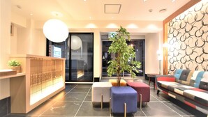 Un hall d’entrée moderne avec un comptoir d’accueil, une grande plante en pot, un canapé agrémenté de coussins colorés et un mur à motifs.