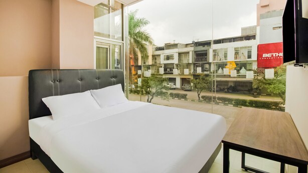A hotel room with a large bed, a wooden nightstand, and a view of the city through a large window. - Collection O Kebon Jeruk Near Paskal 23 Formerly Sentral Paskal (Bandung)
