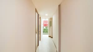 A narrow, well-lit hallway with a tiled floor, leading to a door and a window with a view of greenery outside. - Collection O Kebon Jeruk Near Paskal 23 Formerly Sentral Paskal (Bandung)