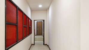 A narrow hallway with red mesh panels on the left, a wooden door at the end, and a tiled floor. - Collection O Kebon Jeruk Near Paskal 23 Formerly Sentral Paskal (Bandung)