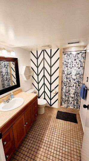 Bathroom features a sink, toilet, and shower area with a floral curtain, set against a chevron-patterned wall and grid-patterned floor.