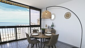 A dining area with a view of the beach, a round table with chairs, a floor lamp, and decorative wall art. - A76 COLON 8C (Calpe)