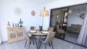 A dining area with a round table, chairs, a wooden cabinet, decorative items, and a view into a living space through a glass door. - A76 COLON 8C (Calpe)