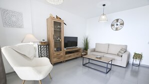 A modern living room with a white sofa, a fluffy chair, a wooden cabinet, a TV, and a coffee table. - A76 COLON 8C (Calpe)