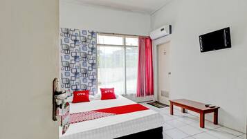A hotel room with a bed, a bedside table, a window with curtains, and a wall-mounted TV.