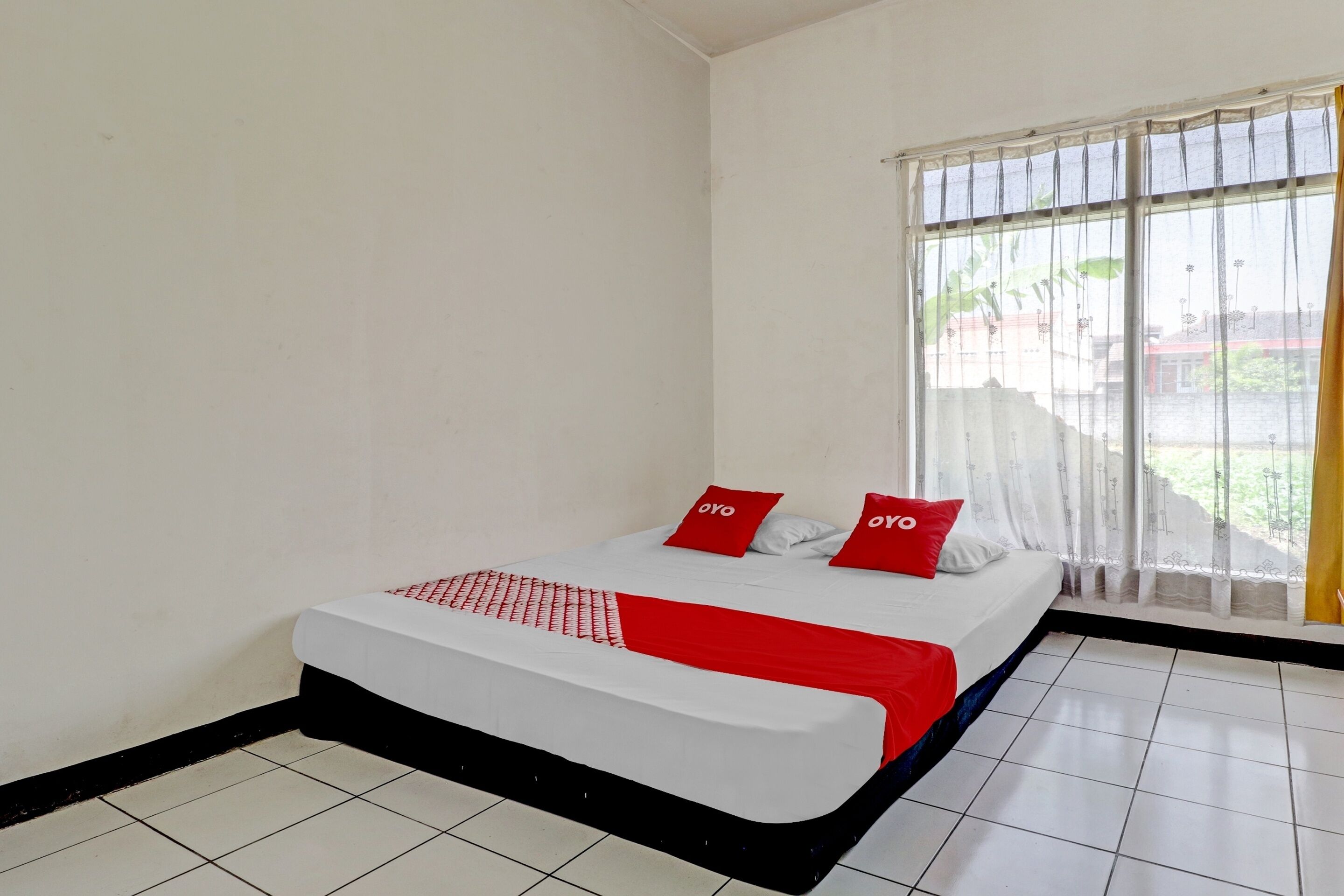 A room with a bed, white walls, and a window with curtains.