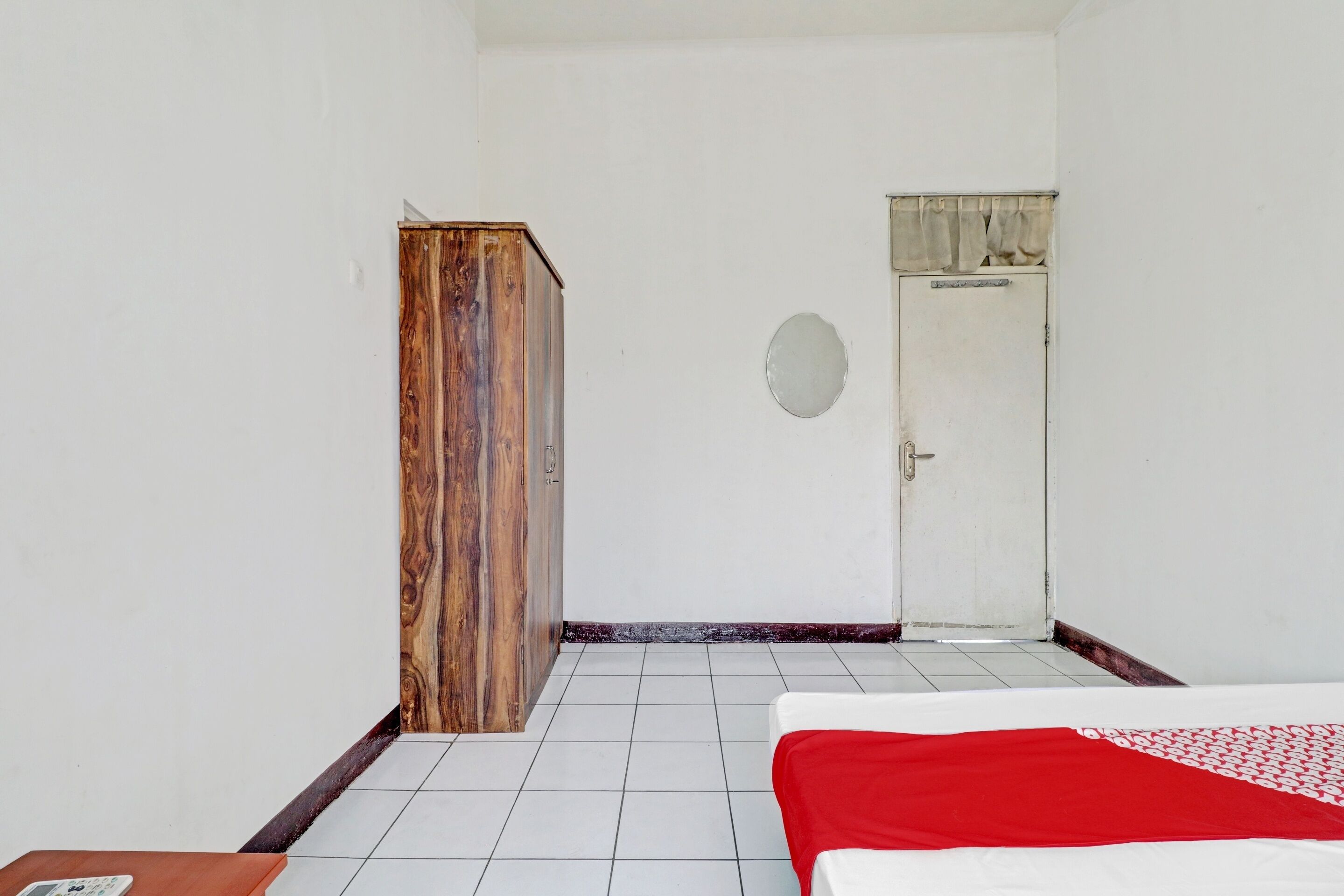 Une pièce avec un lit, une armoire en bois, une porte blanche et un sol carrelé.