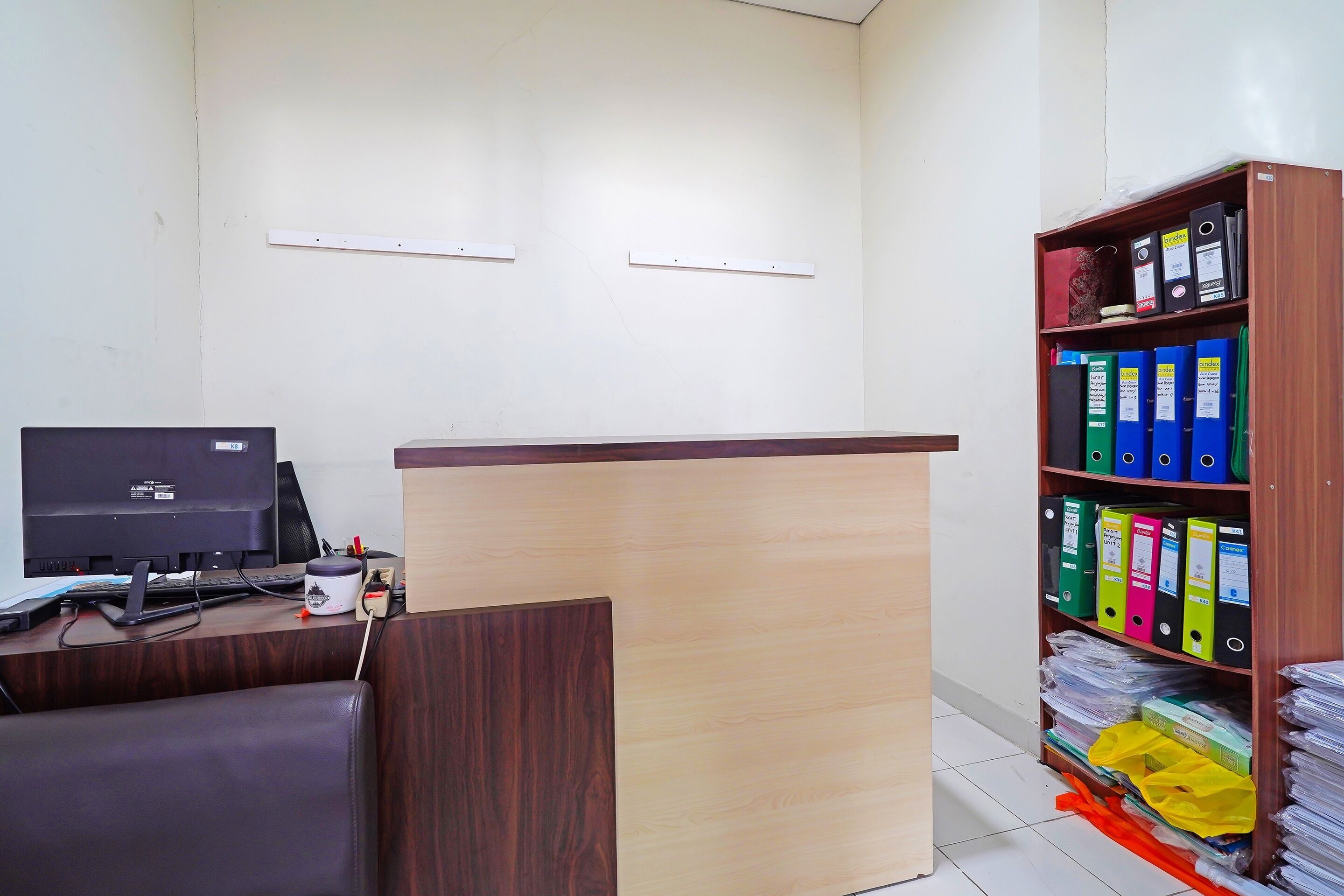 A reception desk with a computer, a chair, and a bookshelf with binders.
