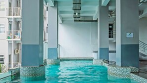 A swimming pool with clear blue water, surrounded by white and gray walls, and supported by large columns. - Collection O 91566 Edurent Bandung (Cileunyi)