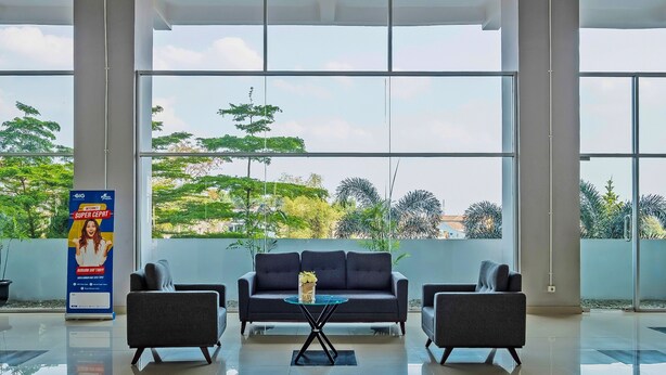 A modern lobby with a sofa and two armchairs, a glass coffee table, and a poster on the wall. - Collection O 91566 Edurent Bandung (Cileunyi)