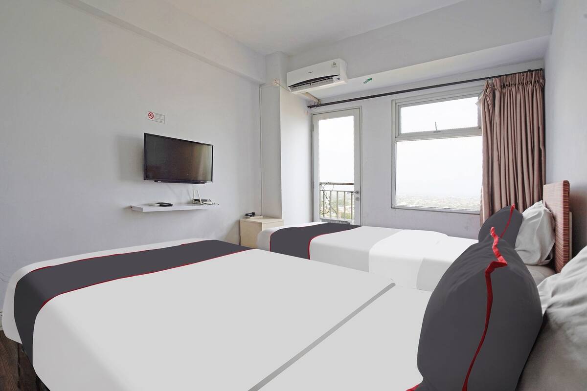 Ein Hotelzimmer mit zwei Betten, einem Fernseher, einer Klimaanlage, einem Fenster mit Vorhängen und einem Balkon.