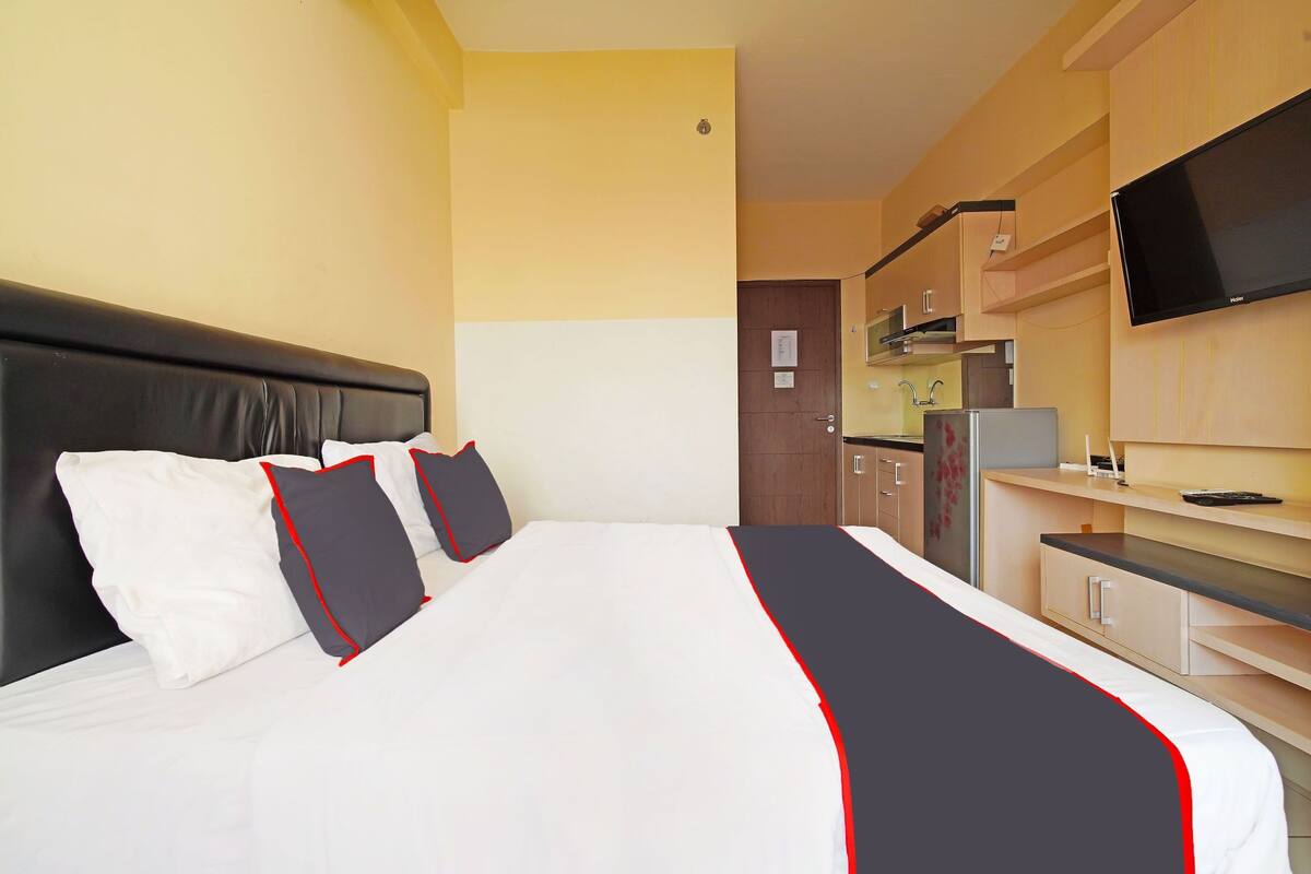 Ein Hotelzimmer mit einem großen Bett, einem Flachbildfernseher, einer Küchenzeile und einer Holztür.