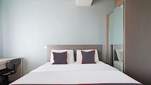 A neatly made bed with white bedding and red trim, two pillows with a black and red design, a wooden headboard, and a mirror on the wall. - Collection O 91566 Edurent Bandung (Cileunyi)
