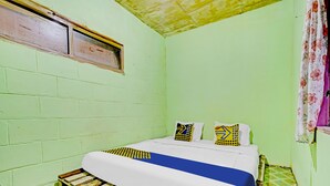 Une petite chambre avec un lit simple, un mur vert, un cadre de lit en bois et un sol à motifs.