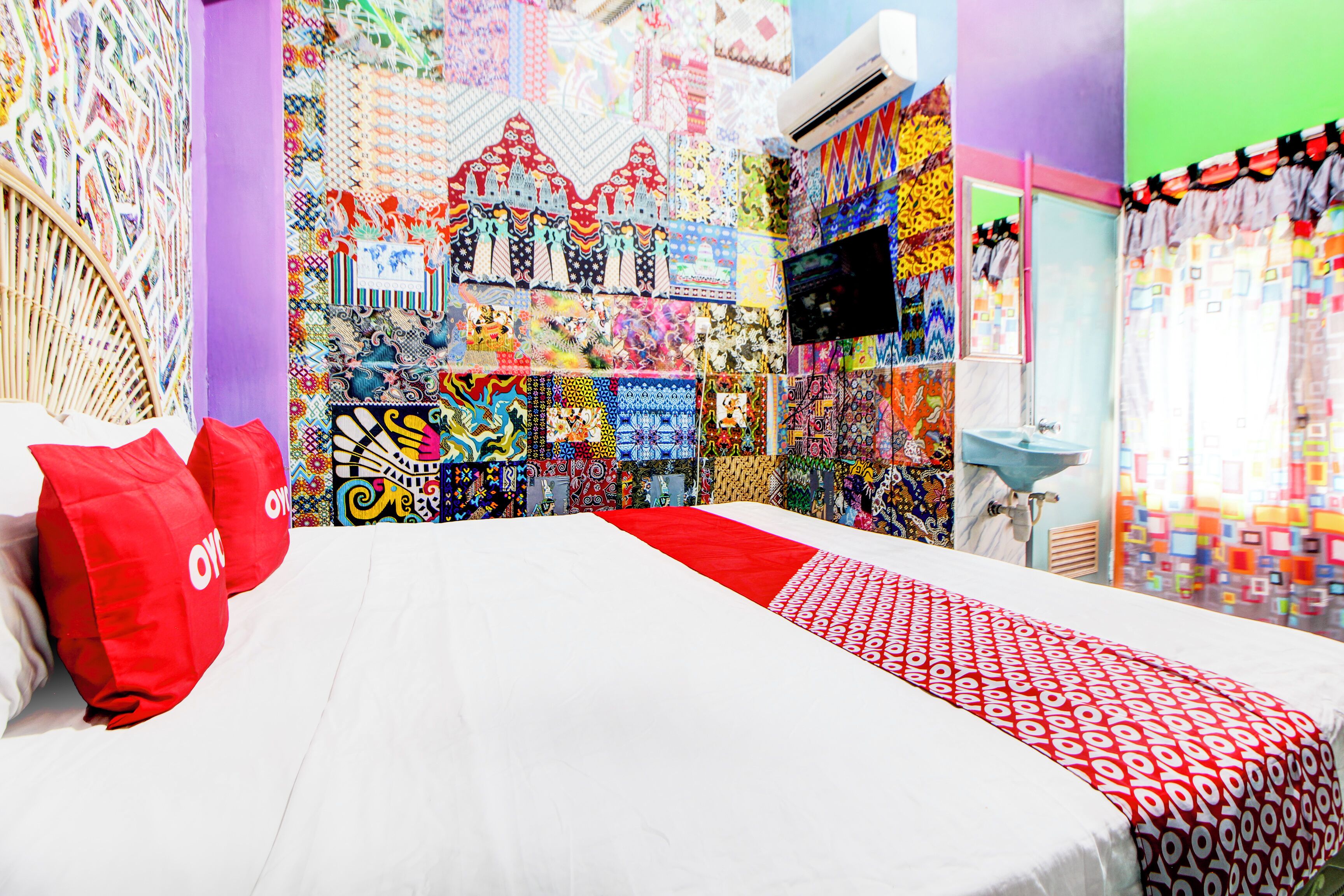 A hotel room with a bed, a TV, and a wall covered with colorful patterns.