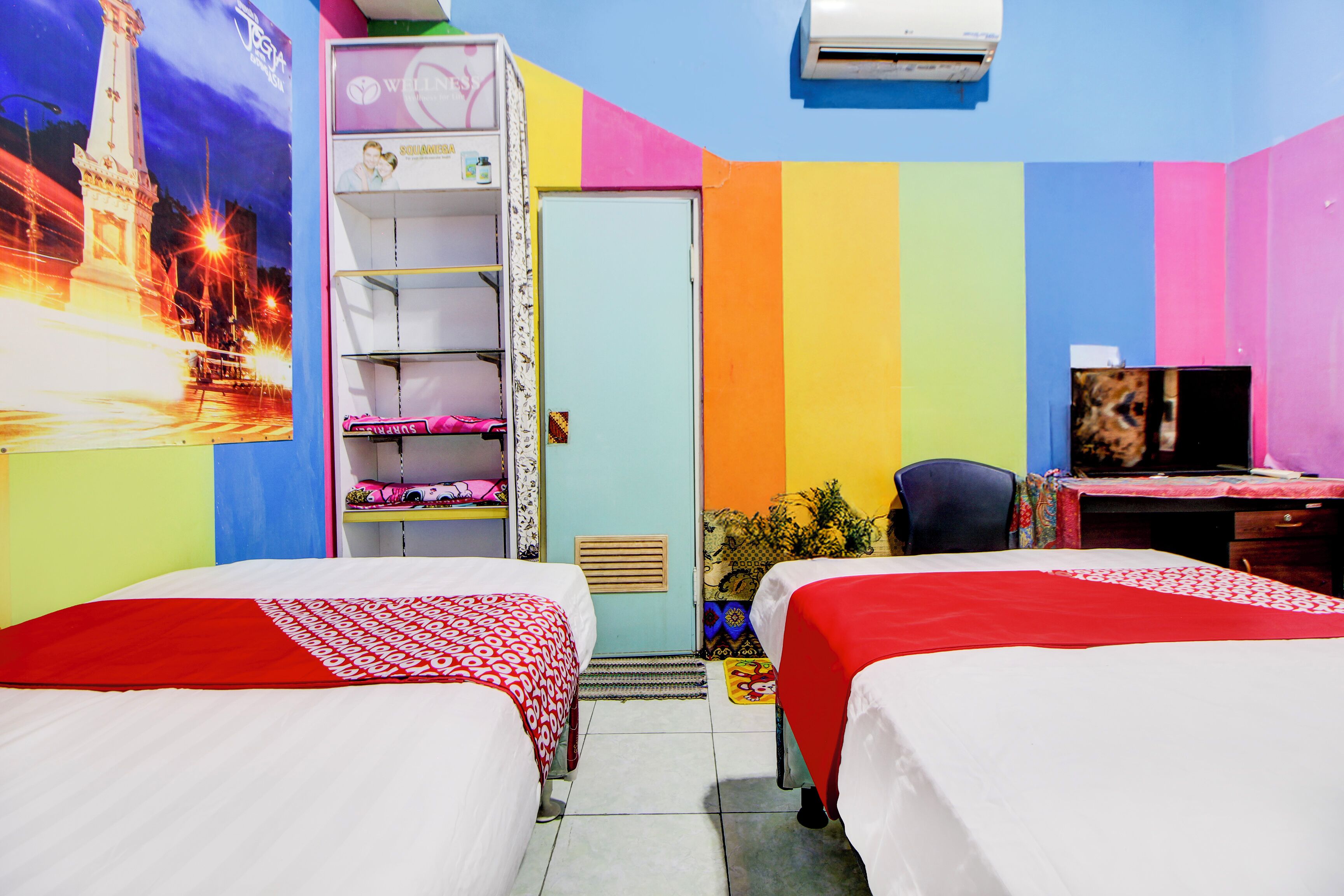 Una habitación con dos camas, televisión, escritorio y un mural colorido.