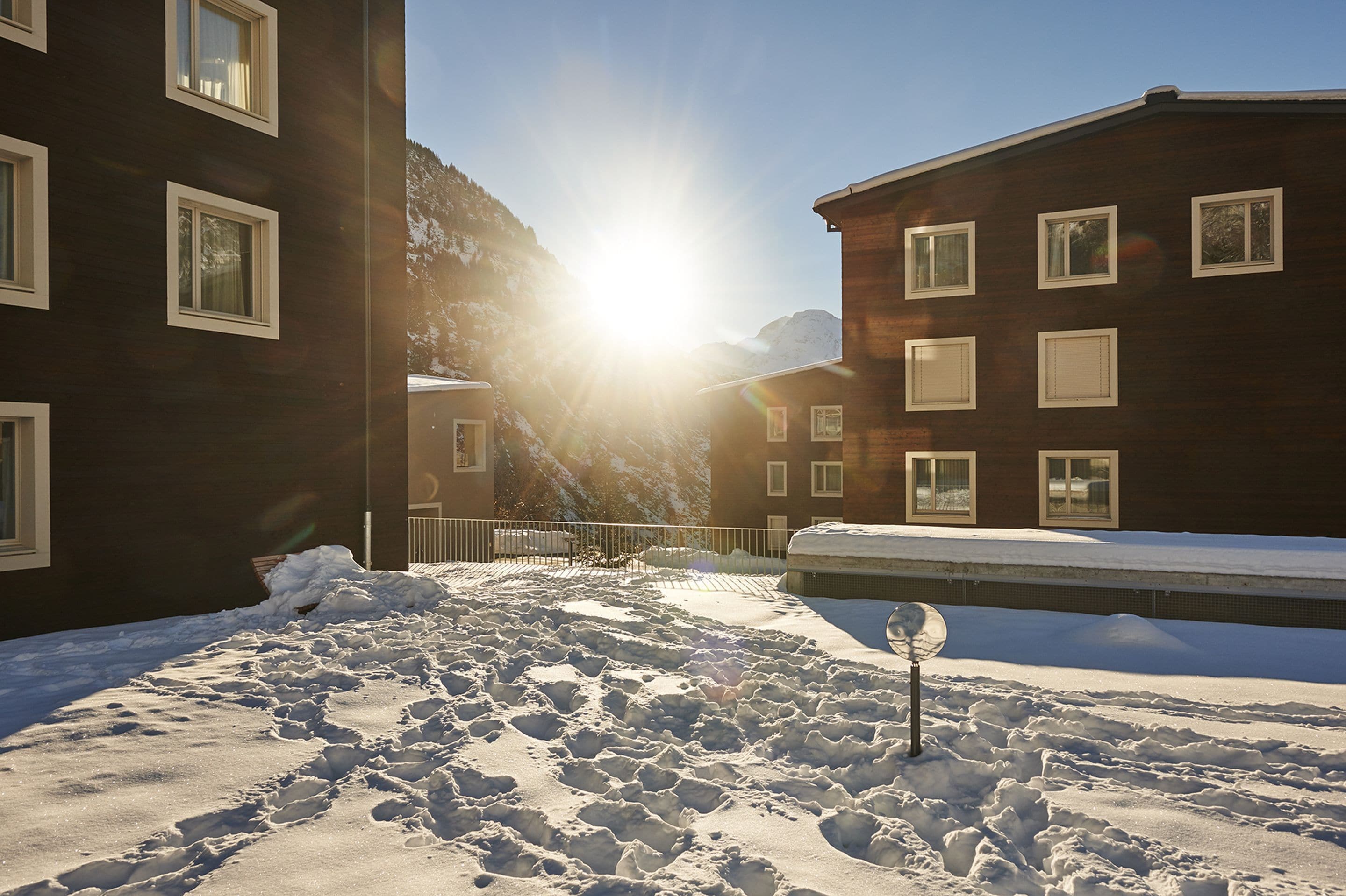 A snowy courtyard with buildings, a metal fence, and a clear sky.