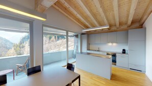 A modern kitchen with a wooden ceiling, large windows offering a mountain view, and a dining area with a table and chairs. - Reka-Feriendorf Blatten-Belalp (Naters)