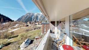 A balcony with a view of a mountainous village, wooden furniture, and a red table. - Reka-Feriendorf Blatten-Belalp (Naters)