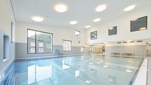A large indoor swimming pool with clear glass walls, multiple windows, and a tiled floor. - Reka-Feriendorf Blatten-Belalp (Naters)